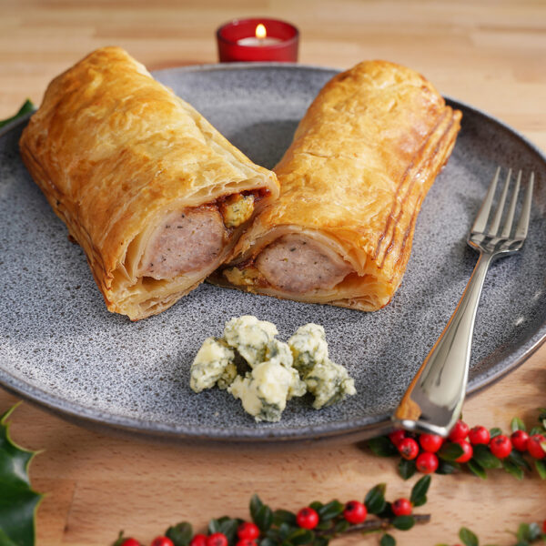 Foot long pork, stilton and onion chutney sausage roll, cut in half on a plate with some stilton cheese